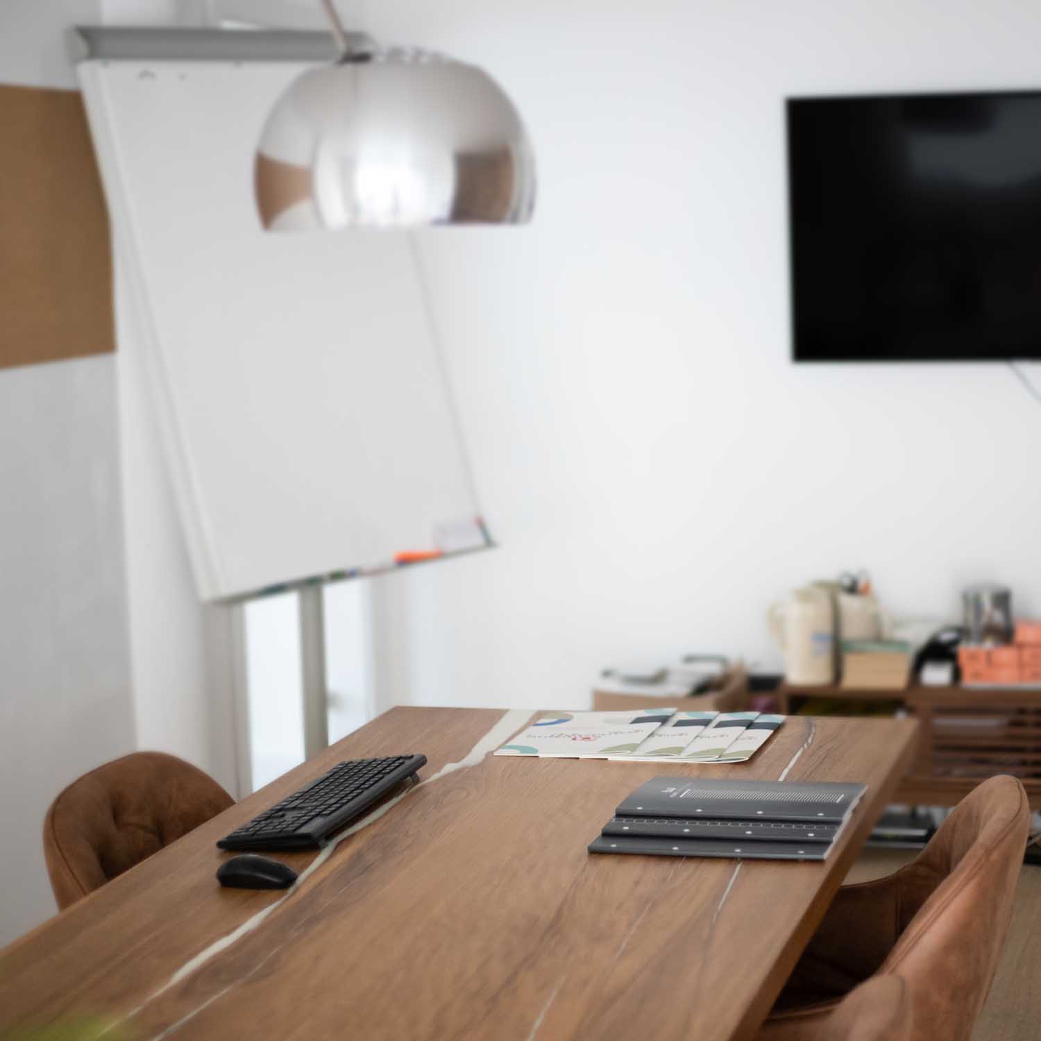 Blick auf einen Konferenztisch mit einer tastaur und an der Wand hängt ein großer Bildschirm